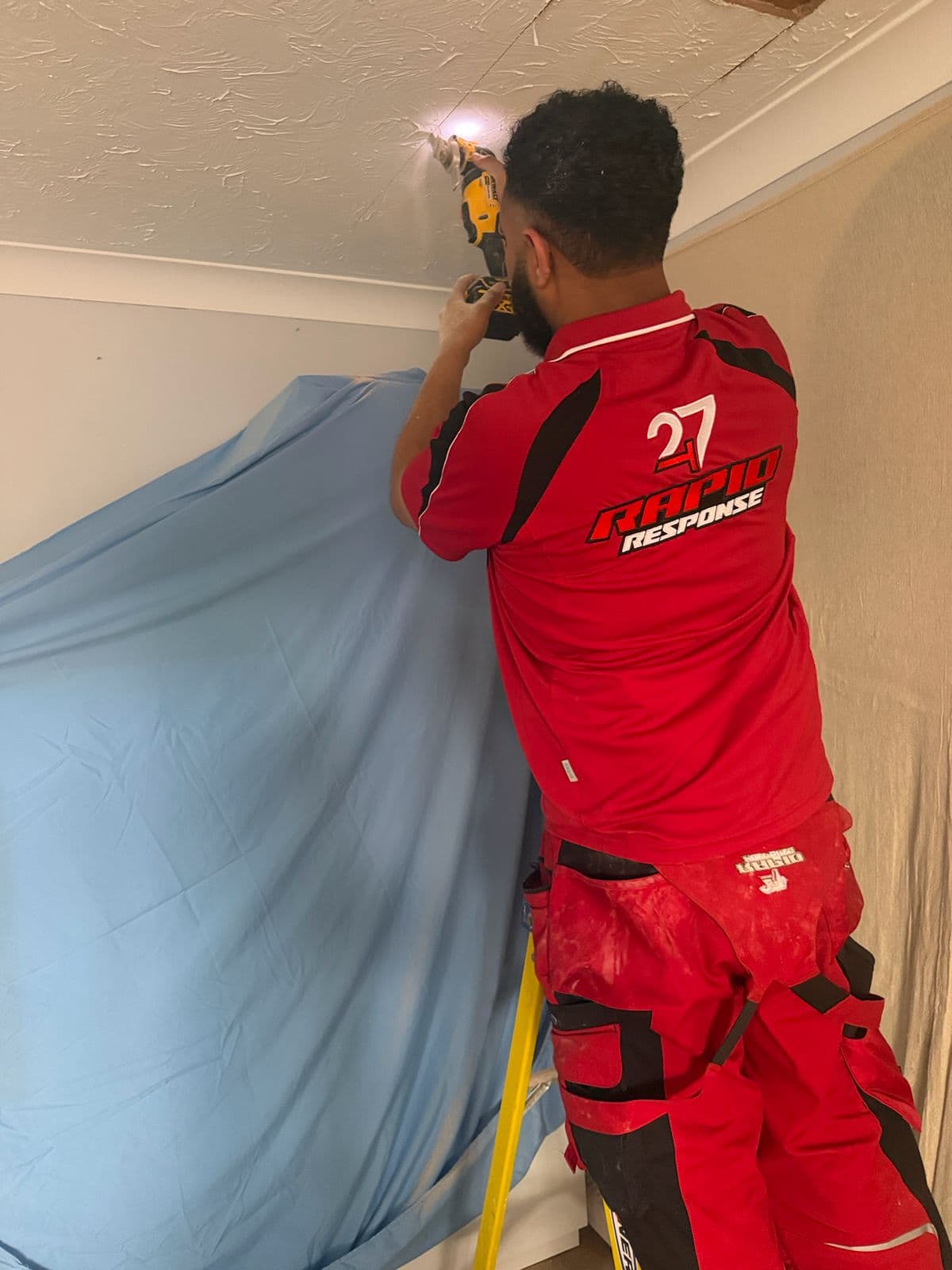 247 Rapid Response engineer on a ladder repairing a ceiling after an upstairs water leak