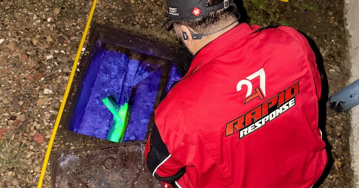 247 Rapid Response engineer surveying an open manhole at night with UV dye visible in the chamber