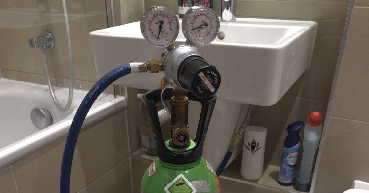 Nitrogen tracer-gas regulator and gauges set up next to a bathroom sink during a leak-detection callout