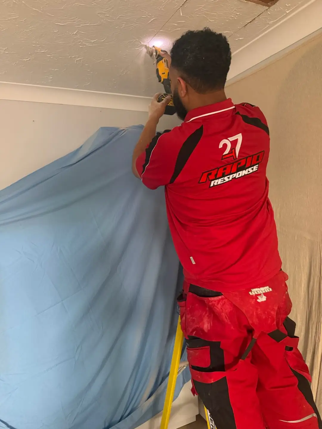 247 Rapid Response engineer on a ladder, drop sheet in place, repairing a ceiling after an upstairs water leak